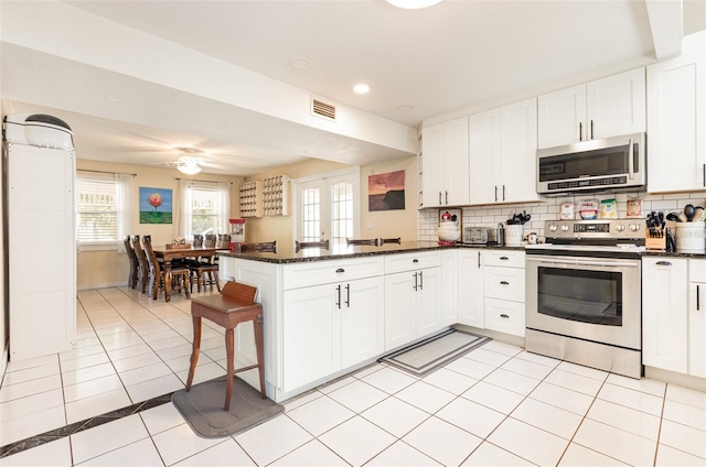 kitchen featuring a peninsula, light tile patterned floors, stainless steel appliances, white cabinetry, and visible vents