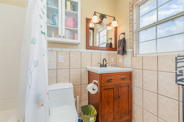 bathroom featuring tile walls, toilet, a shower with shower curtain, vanity, and a wainscoted wall