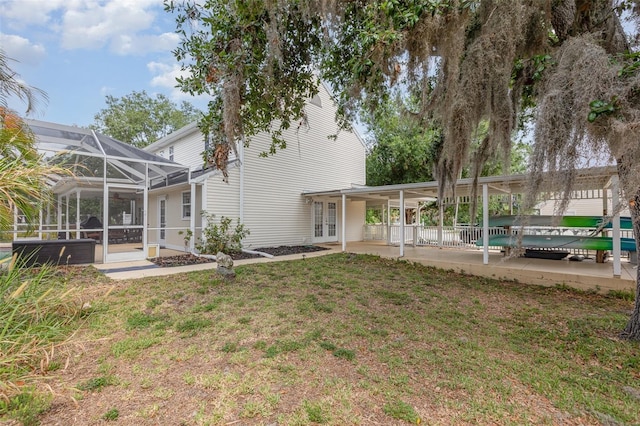 back of property featuring french doors, an attached carport, a lawn, a patio area, and glass enclosure