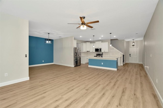kitchen with ceiling fan with notable chandelier, open floor plan, light countertops, appliances with stainless steel finishes, and backsplash