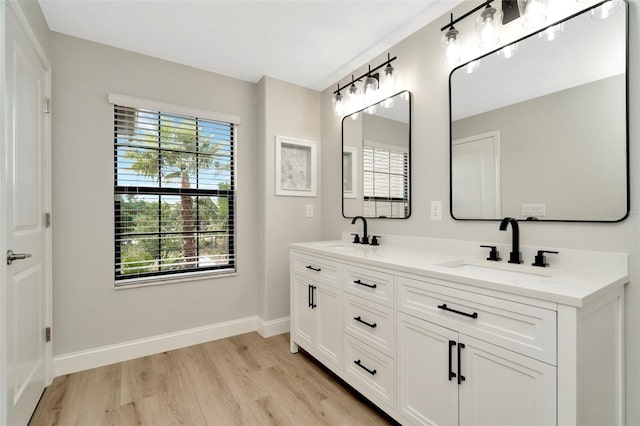bathroom featuring a sink, baseboards, double vanity, and wood finished floors