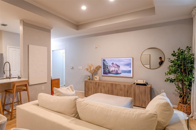 living room with visible vents, crown molding, a raised ceiling, baseboards, and light wood-style flooring