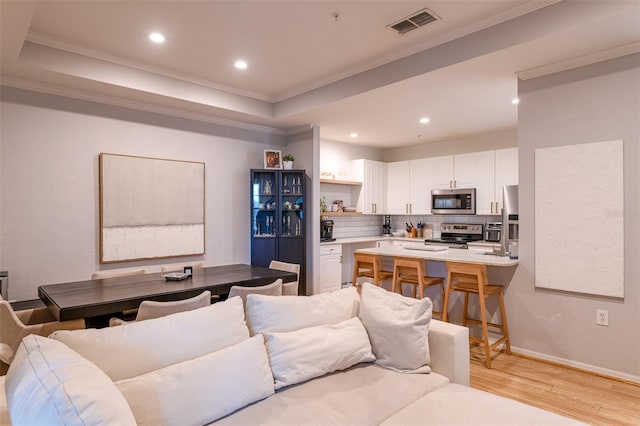 living area featuring crown molding, a raised ceiling, light wood finished floors, recessed lighting, and visible vents