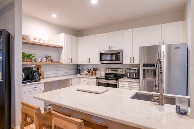 kitchen with white cabinets, open shelves, appliances with stainless steel finishes, light stone counters, and a kitchen breakfast bar