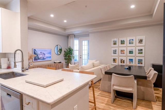 kitchen featuring a kitchen bar, stainless steel dishwasher, a sink, a raised ceiling, and light wood-style flooring