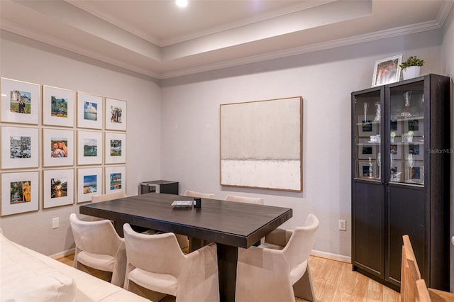 dining space featuring crown molding, a raised ceiling, light wood finished floors, and baseboards