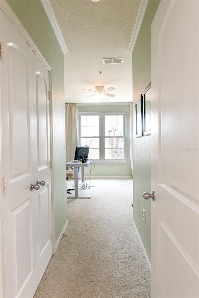 hallway featuring visible vents, carpet, crown molding, and baseboards