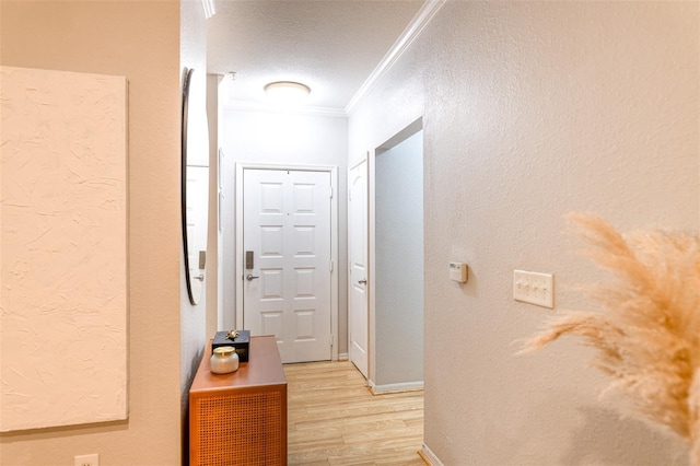 hall with a textured wall, light wood finished floors, a textured ceiling, baseboards, and ornamental molding