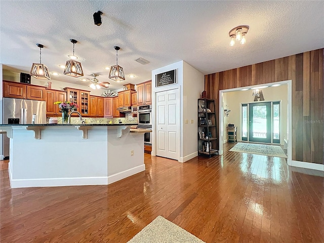 16224 Iola Woods Trl, Dade City, FL 33523 - kitchen with brown cabinetry, visible vents, a breakfast bar, a textured ceiling, and stainless steel appliances