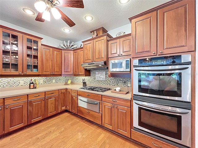 16224 Iola Woods Trl, Dade City, FL 33523 - kitchen with appliances with stainless steel finishes, light countertops, light wood-type flooring, under cabinet range hood, and a warming drawer