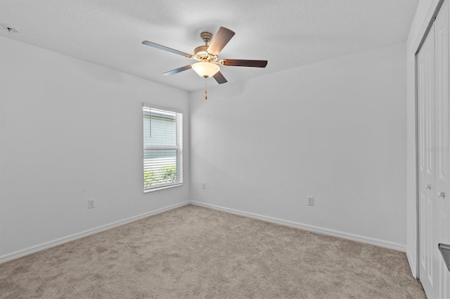spare room featuring a ceiling fan, baseboards, and light carpet