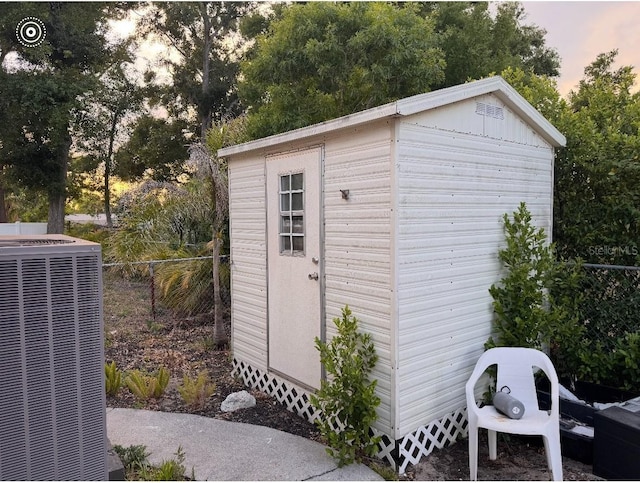 outdoor structure at dusk with a storage shed, fence, central AC unit, and an outbuilding