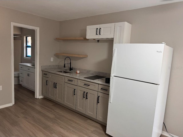 kitchen with open shelves, freestanding refrigerator, a sink, and light wood-style floors