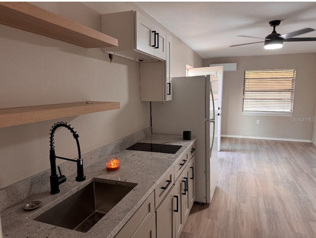kitchen with a ceiling fan, light stone countertops, black electric cooktop, a sink, and light wood-style floors