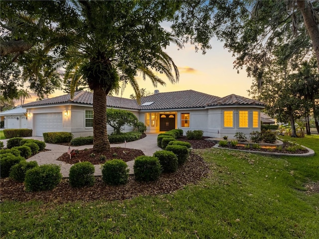 view of front of home featuring an attached garage, a tiled roof, stucco siding, and a front lawn
