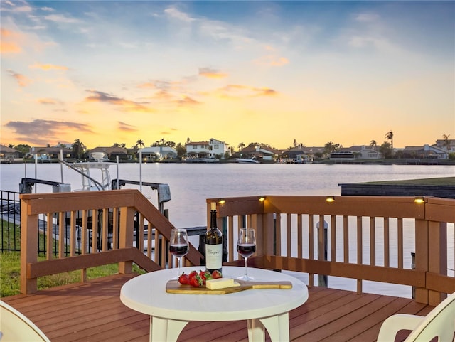 deck at dusk featuring a water view, a dock, and a residential view