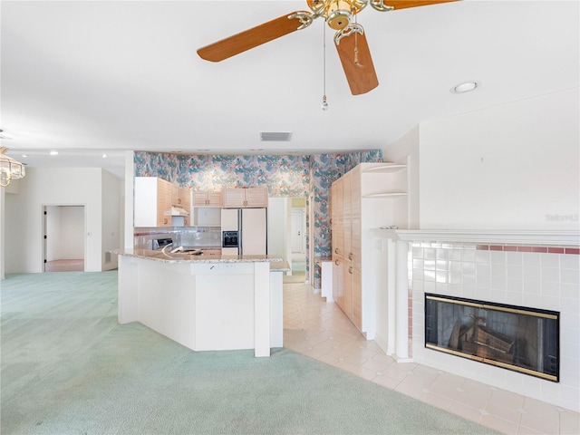 kitchen featuring white fridge with ice dispenser, visible vents, ceiling fan, light colored carpet, and light stone counters