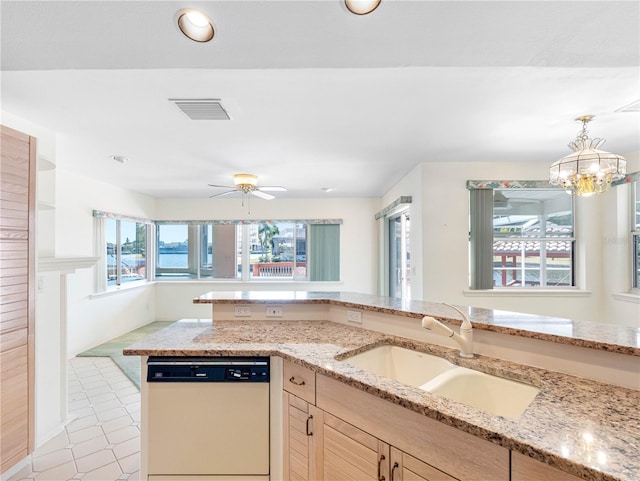 kitchen with a sink, decorative light fixtures, light stone counters, visible vents, and white dishwasher