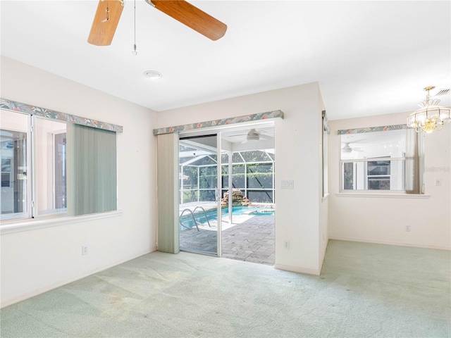 carpeted empty room featuring a sunroom, ceiling fan with notable chandelier, and baseboards