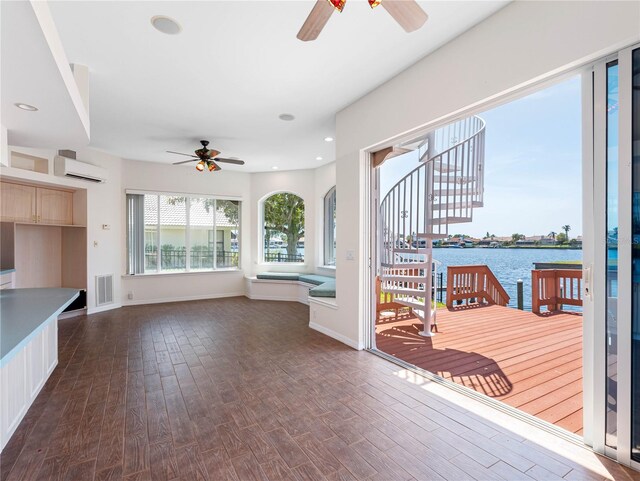 unfurnished living room with a wall mounted air conditioner, dark wood finished floors, ceiling fan, visible vents, and a water view