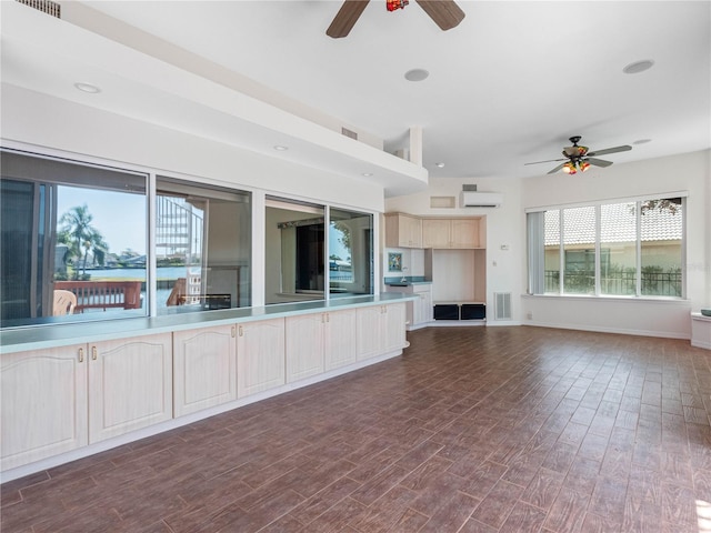 unfurnished living room with a ceiling fan, a wall mounted air conditioner, visible vents, baseboards, and dark wood-style flooring