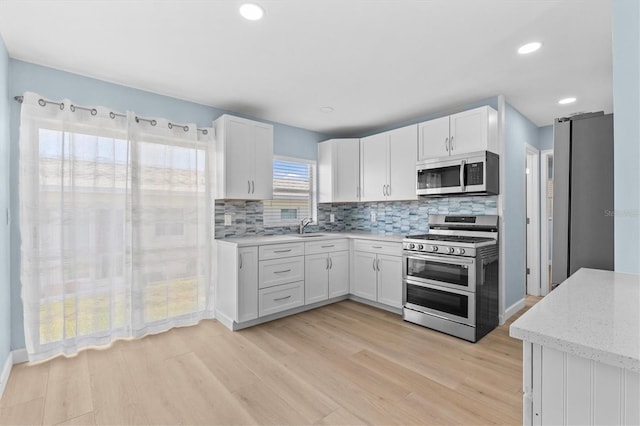12400 Park Blvd Unit 210, Seminole, FL 33772 - kitchen featuring white cabinetry, tasteful backsplash, a sink, light wood finished floors, and stainless steel appliances