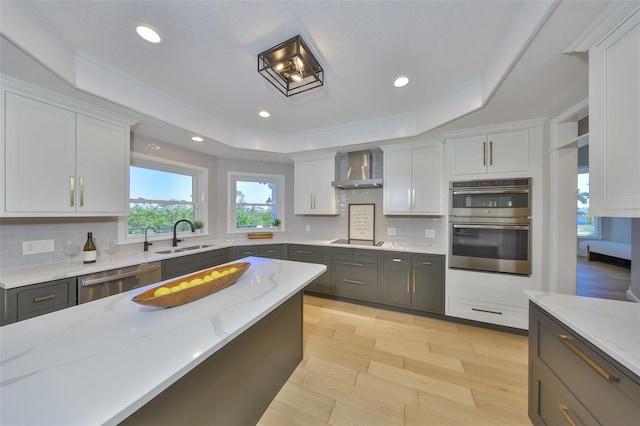 945 Bunker View Dr, Apollo Beach, FL 33572 - kitchen featuring wall chimney range hood, a raised ceiling, light stone counters, a sink, and stainless steel appliances