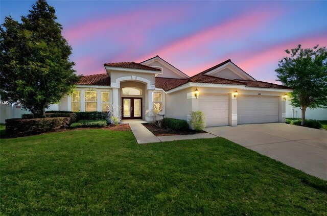 mediterranean / spanish house with a lawn, stucco siding, french doors, an attached garage, and driveway