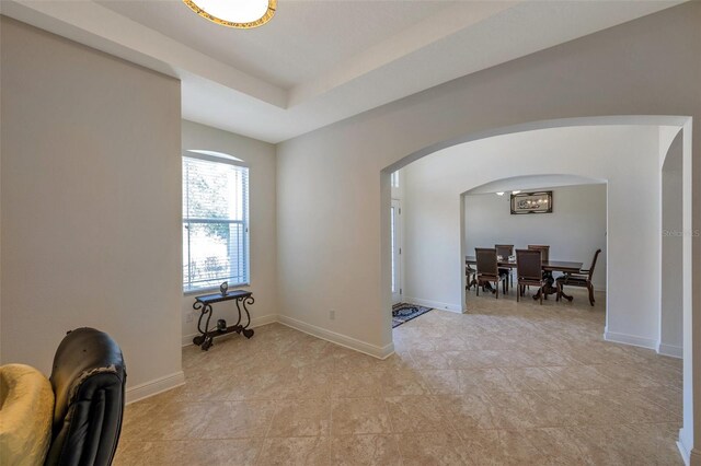 unfurnished room featuring light tile patterned floors, arched walkways, and baseboards