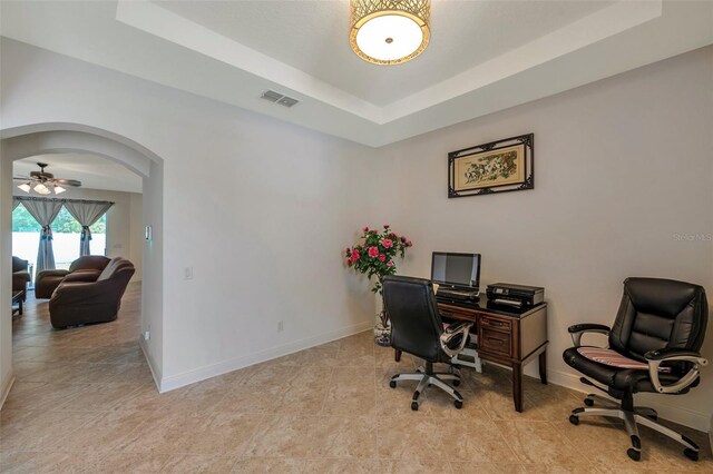 home office featuring arched walkways, a ceiling fan, baseboards, a tray ceiling, and visible vents