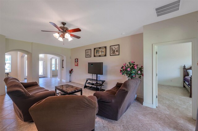 living room featuring a ceiling fan, visible vents, arched walkways, baseboards, and light tile patterned flooring