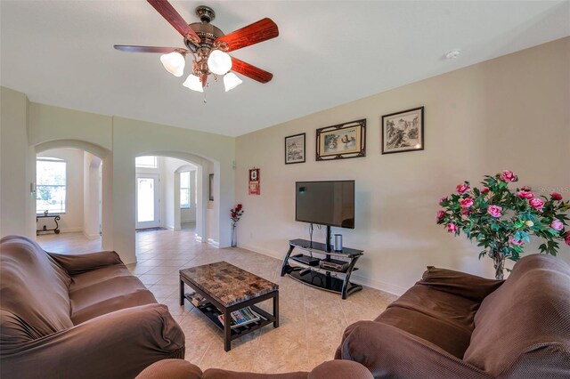 living room featuring baseboards, arched walkways, a ceiling fan, and light tile patterned floors