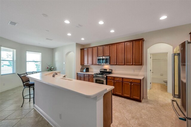 kitchen with arched walkways, light countertops, stainless steel appliances, recessed lighting, and an island with sink