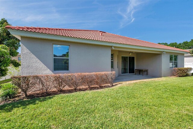 rear view of house with a yard, a tile roof, a patio area, and stucco siding