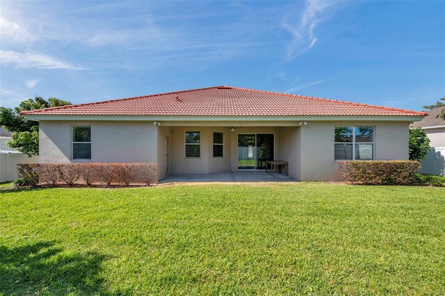 rear view of house featuring a lawn, stucco siding, a patio area, and a tile roof