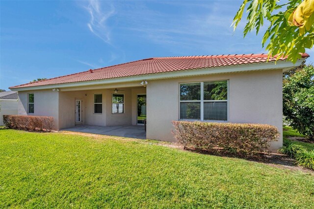 rear view of property with a tile roof, stucco siding, a patio area, a ceiling fan, and a yard