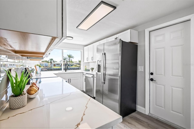 kitchen with white cabinets, appliances with stainless steel finishes, light stone counters, a sink, and light wood-style floors