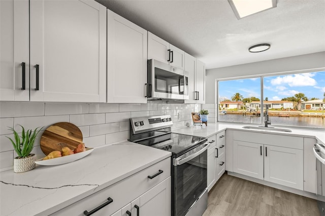 12700 5th Isle, Hudson, FL 34667 - kitchen featuring appliances with stainless steel finishes, a sink, light wood finished floors, white cabinetry, and decorative backsplash