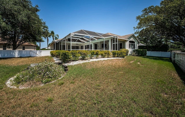 rear view of house with a fenced backyard, glass enclosure, and a lawn