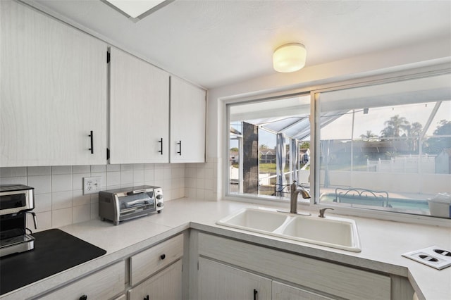 kitchen featuring light countertops, a toaster, decorative backsplash, and a sink