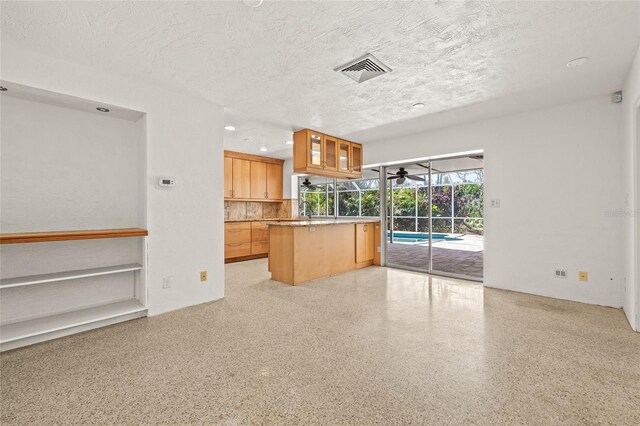 1141 80th Street Ct S, Saint Petersburg, FL 33707 - kitchen with a textured ceiling, dark aggregate flooring, ceiling fan, glass insert cabinets, and a kitchen island