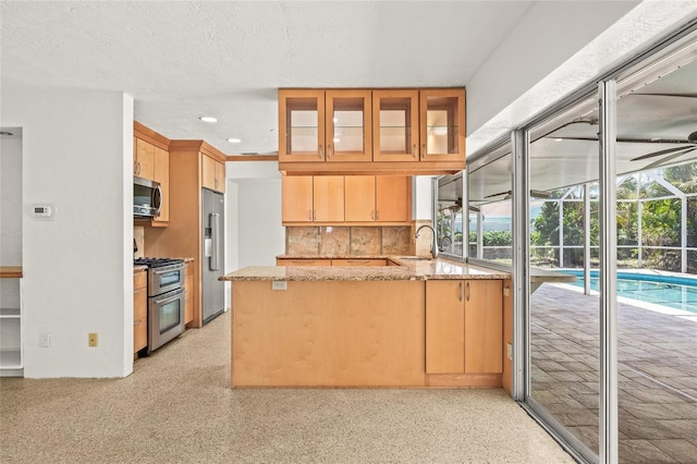 1141 80th Street Ct S, Saint Petersburg, FL 33707 - kitchen featuring appliances with stainless steel finishes, a peninsula, light stone countertops, tasteful backsplash, and a sink