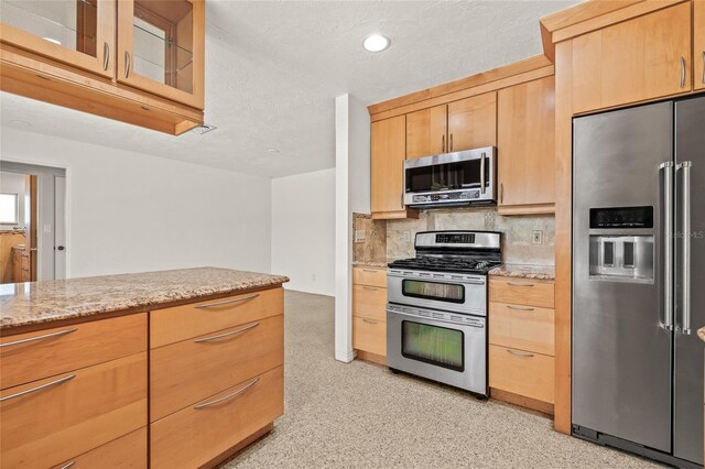 1141 80th Street Ct S, Saint Petersburg, FL 33707 - kitchen with appliances with stainless steel finishes, tasteful backsplash, light stone countertops, glass insert cabinets, and light brown cabinets