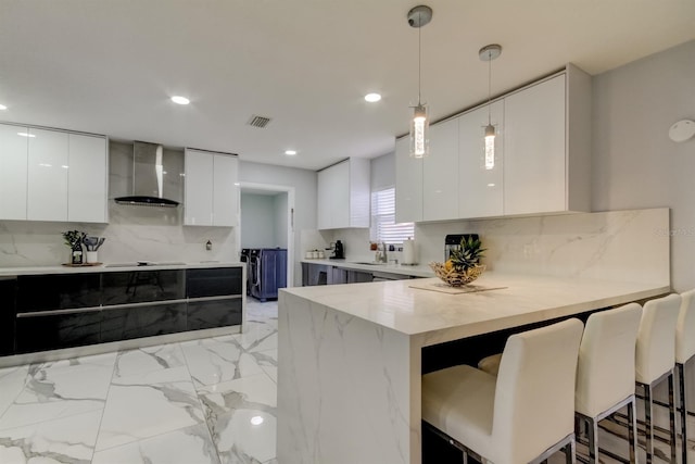 kitchen featuring modern cabinets, a breakfast bar, a peninsula, and wall chimney exhaust hood