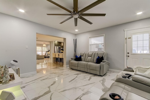 living area featuring baseboards, a ceiling fan, and a wealth of natural light