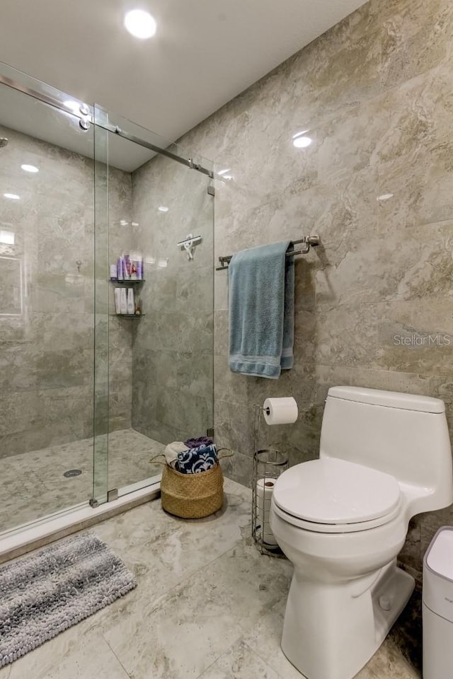 bathroom with toilet, tile walls, a shower stall, and marble finish floor