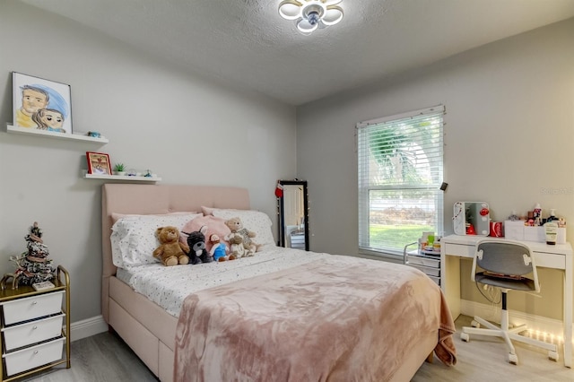 bedroom featuring a textured ceiling, baseboards, and light wood-style flooring