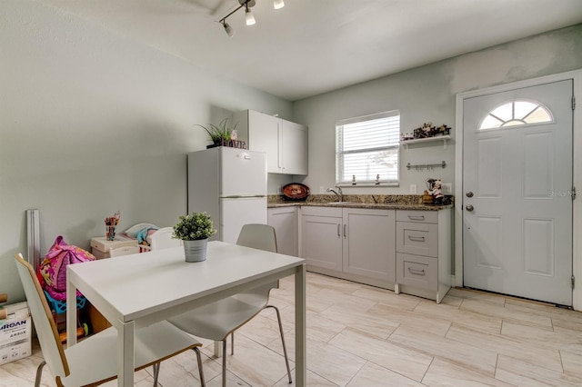 kitchen with freestanding refrigerator, open shelves, a sink, and dark stone counters