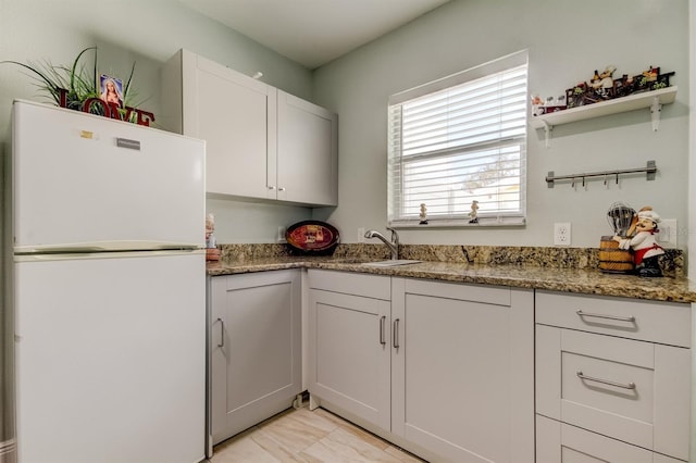 kitchen with freestanding refrigerator, open shelves, stone countertops, and a sink