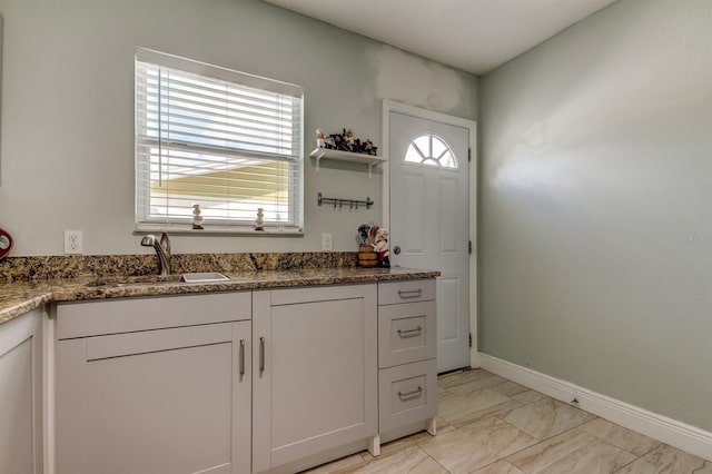 kitchen with a sink, marble finish floor, white cabinetry, baseboards, and stone counters